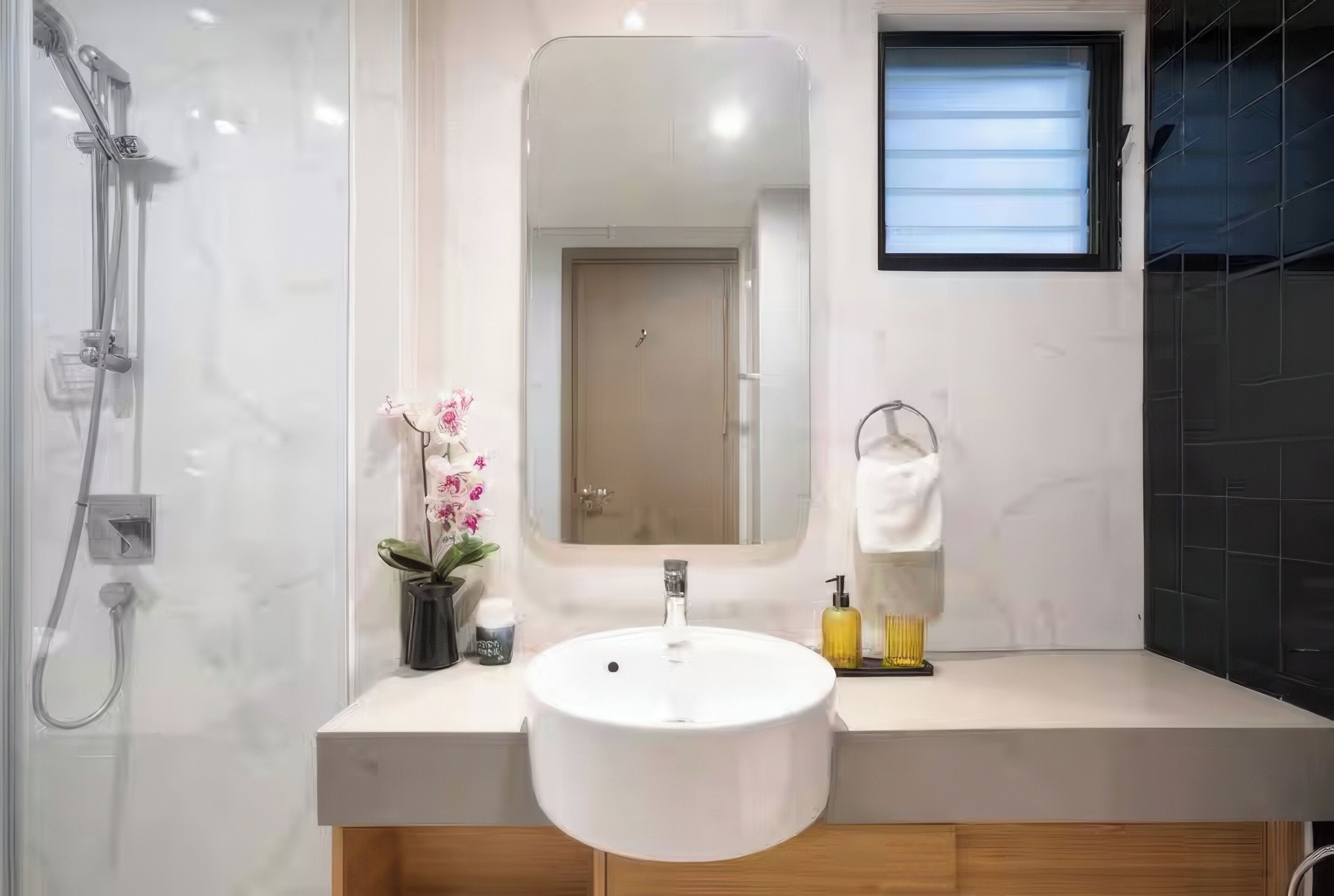 Une salle de bain moderne avec un lavabo blanc, un miroir, une douche et une petite fenêtre.