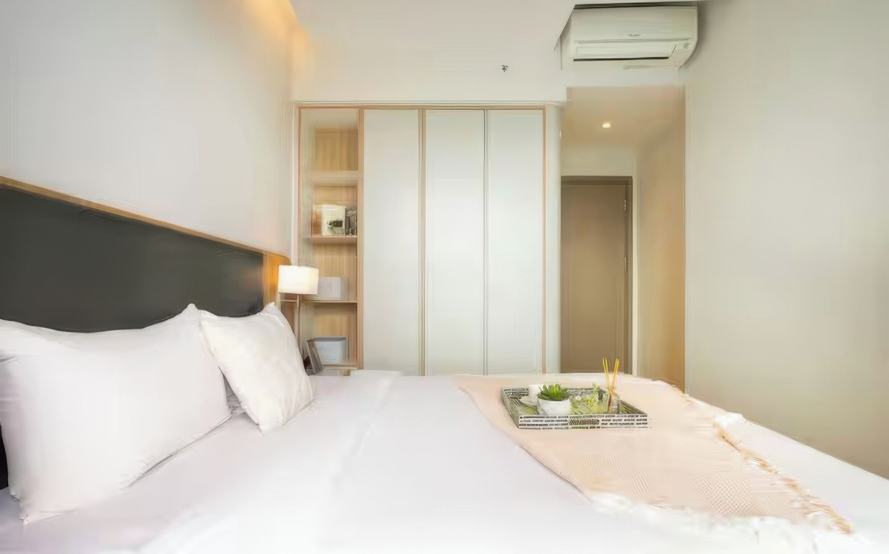 A hotel room with a bed, a bedside lamp, a small table with a tray, and a wardrobe.