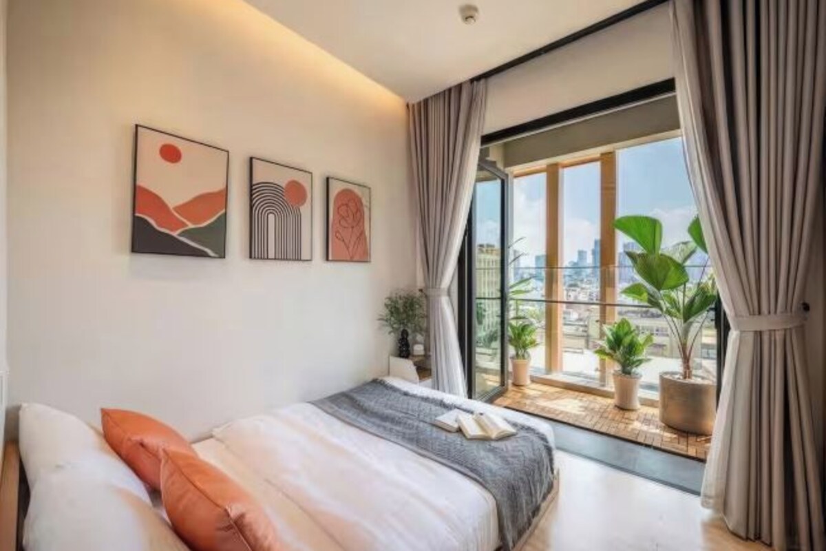 A modern bedroom with a large window, a bed with pillows, and three wall-mounted artworks.