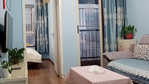 Quarto com cama, mesa de cabeceira, televisão e janela com cortinas.