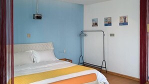 Quarto de hotel com cama, projetor, cabideiro e obras de arte nas paredes.
