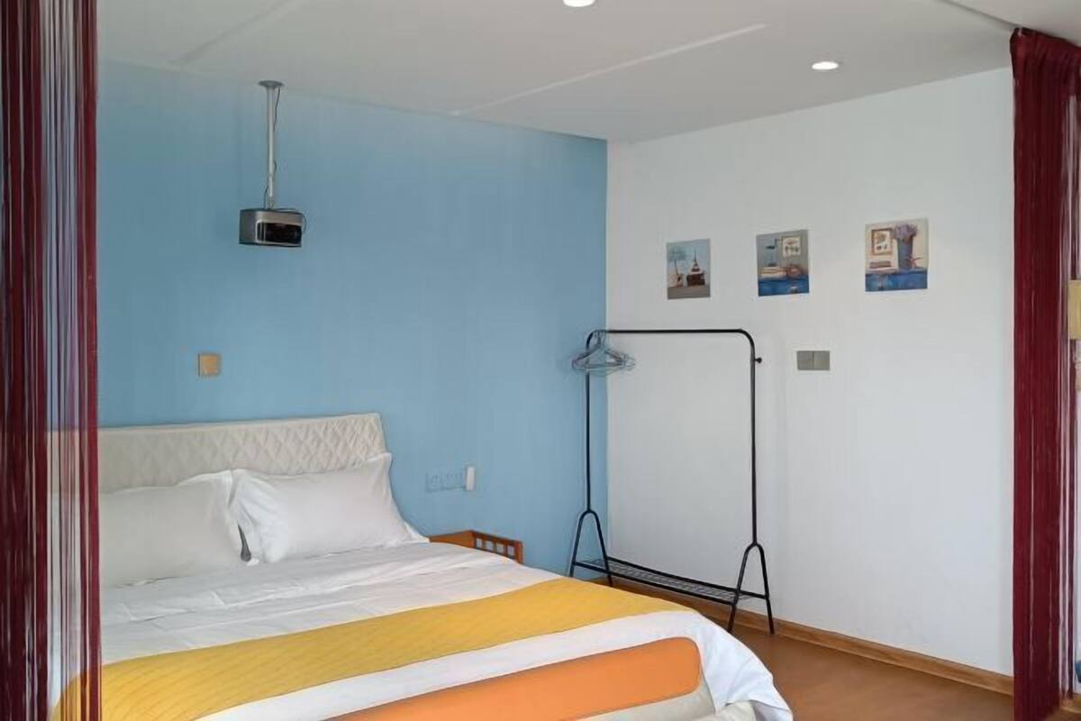 Een hotelkamer met een bed, een beamer, een kapstok en wanddecoratie.