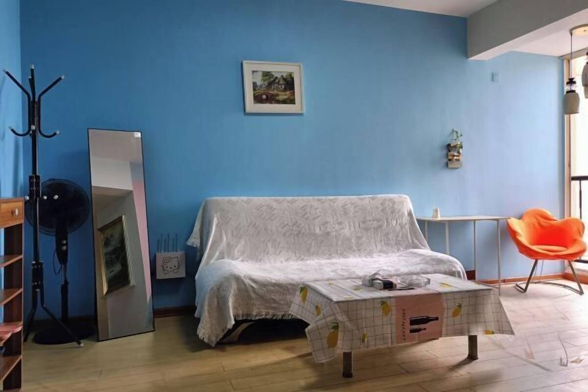 Een kamer met een bed, een tafel met tafelkleed, een stoel, een spiegel en een ventilator.