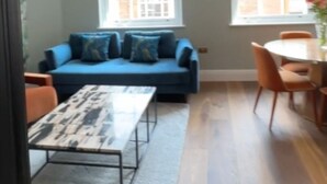 Een moderne woonkamer met een blauwe bank, een tafel met een patroon erop en een eethoek met een tafel en stoelen.