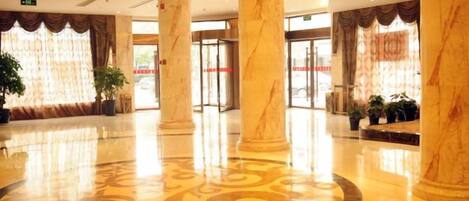 Un vestíbulo con columnas de mármol, piso estampado y una recepción con puerta de cristal.