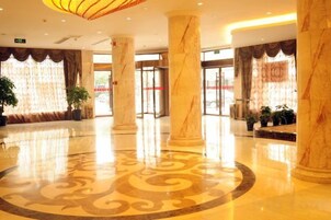 Un vestíbulo con columnas de mármol, piso estampado y una recepción con puerta de cristal.