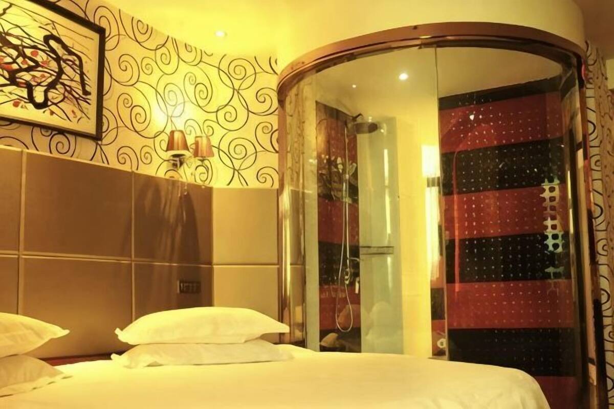 A hotel room with a bed, a curved mirror, a shower, and a patterned wall.