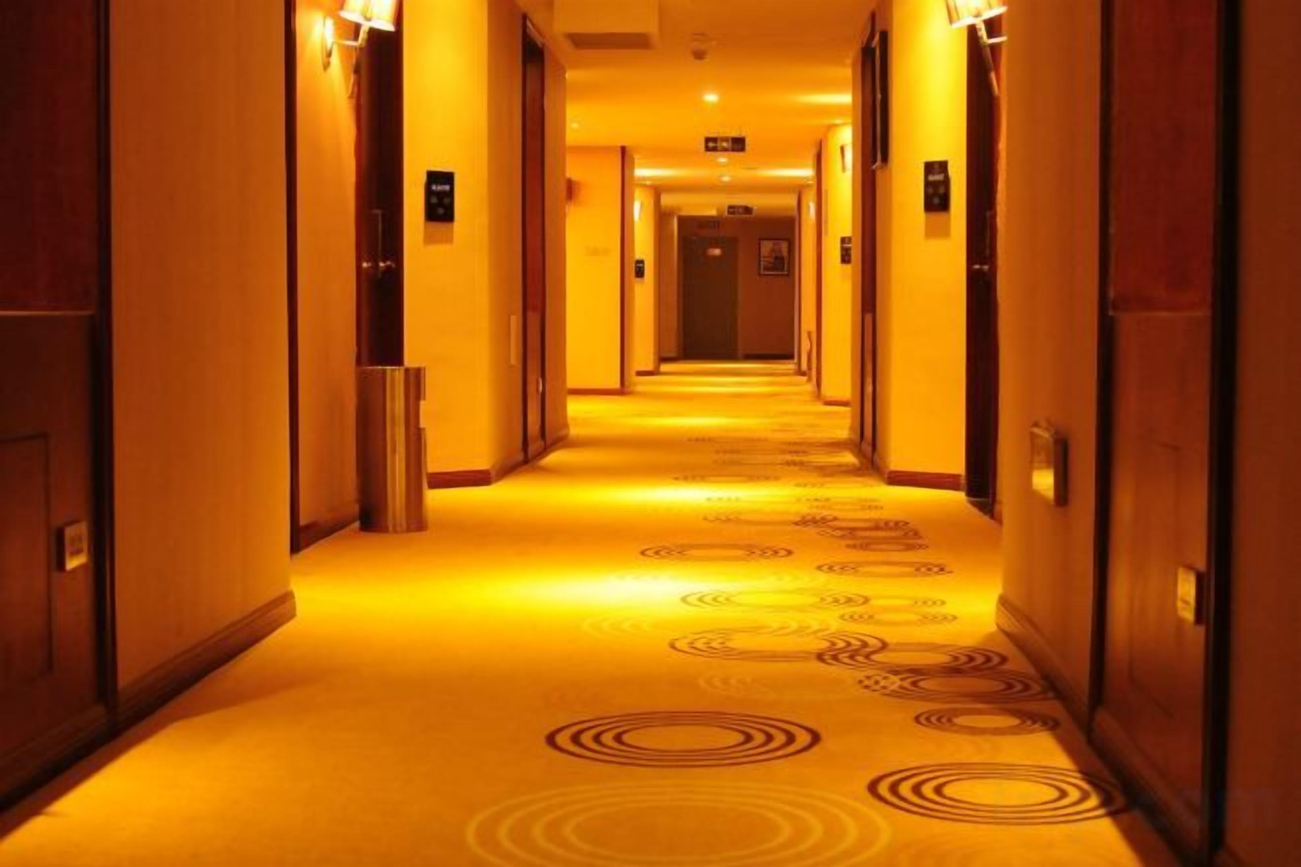 Un pasillo de hotel con puertas a ambos lados, alfombra estampada e iluminación en el techo.
