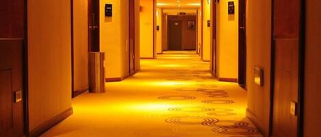 A hotel corridor with doors on both sides, a patterned carpet, and overhead lighting.