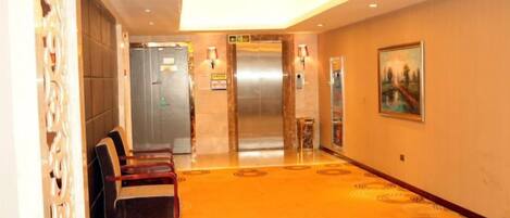 A hotel lobby with a carpeted floor, a reception desk, an elevator, and a wall-mounted painting.