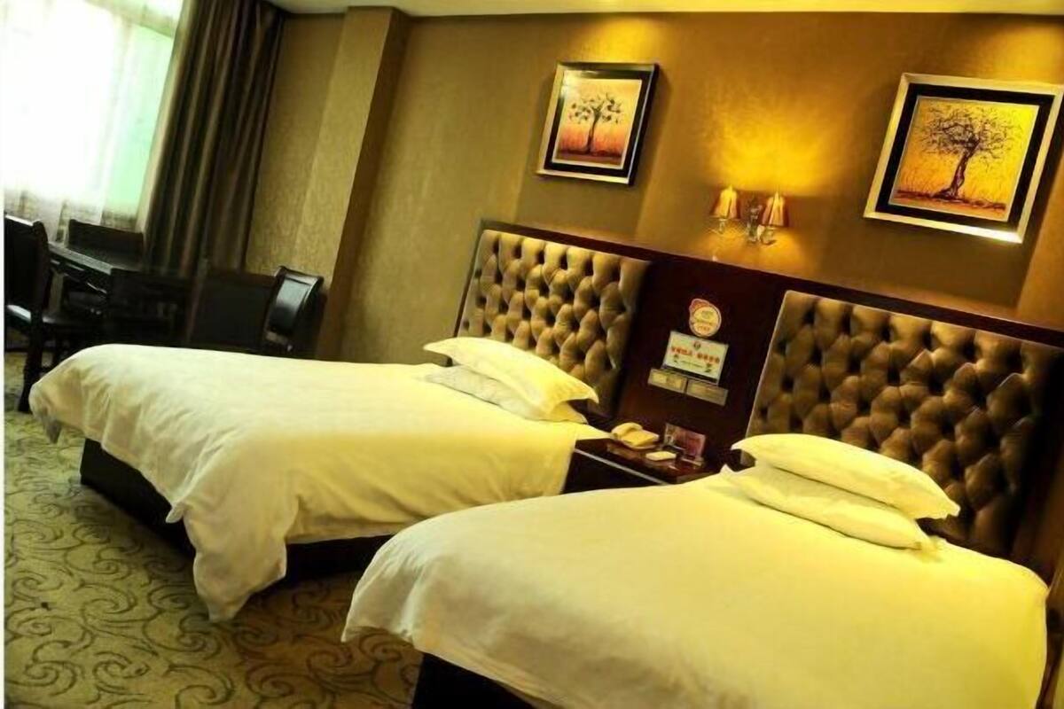 A hotel room with two beds, a desk, and a chair. There are framed pictures on the wall and a clock on the nightstand.