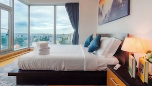 A modern hotel room with a large bed, a nightstand, a lamp, and a painting on the wall.