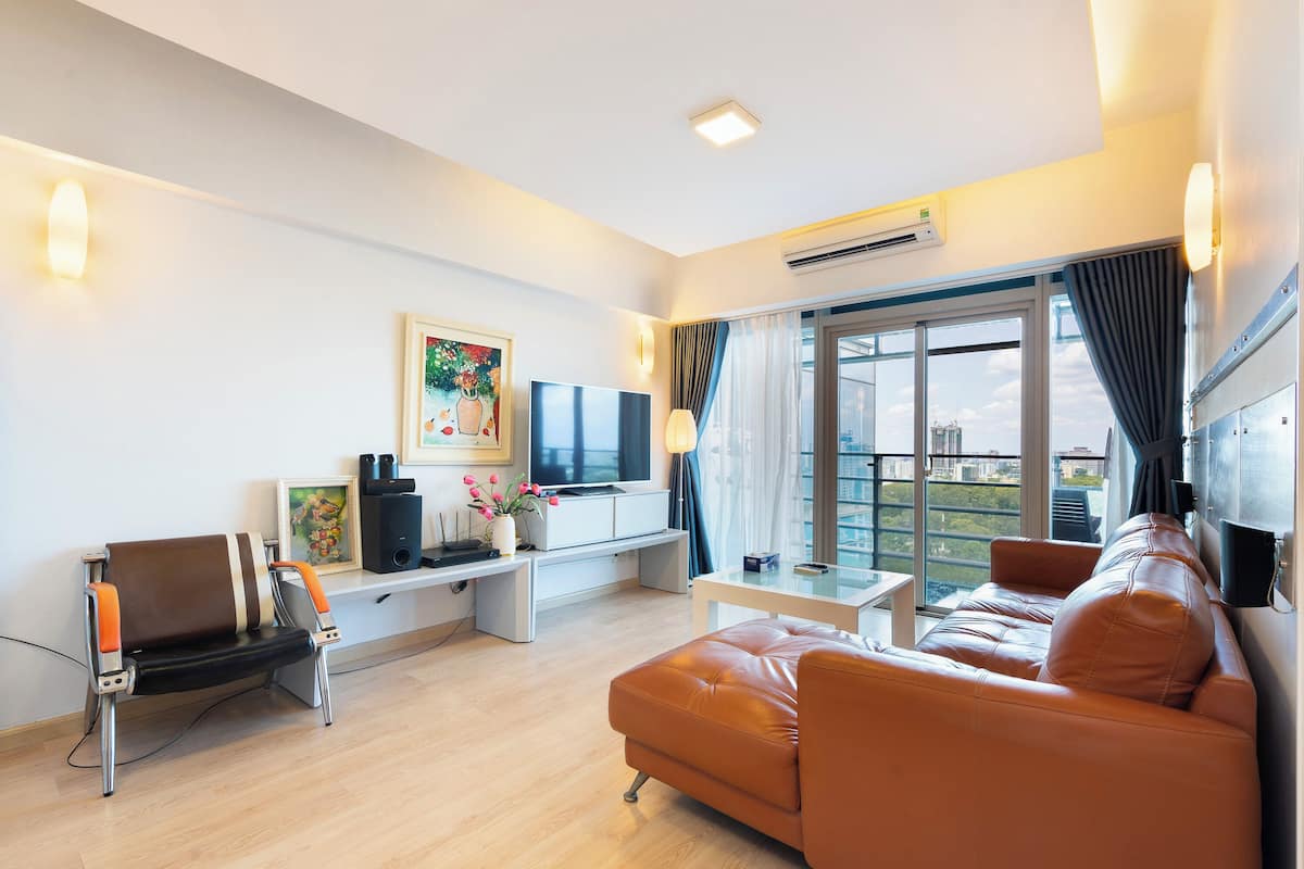 Ein modernes Wohnzimmer mit einer Couch, einem Fernseher, einem Schreibtisch und einem großen Fenster mit Vorhängen.
