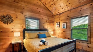 A wooden cabin bedroom with a bed, two bedside tables, a window, and a wall decoration. - 
Smoky Mountain Cabin; 3 King Suites; Hot Tub; Game Room; Sleeps 12 (Sevierville)