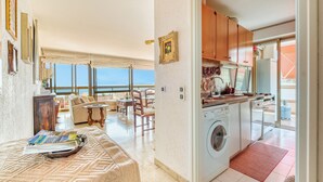 A living area with a sofa, a dining table, and a kitchen with a washing machine.