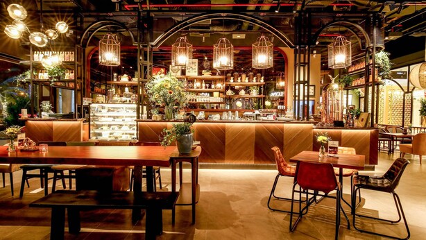 Un restaurante acogedor con mesas y sillas de madera, una zona de bar con estantes llenos de botellas y lámparas colgantes.