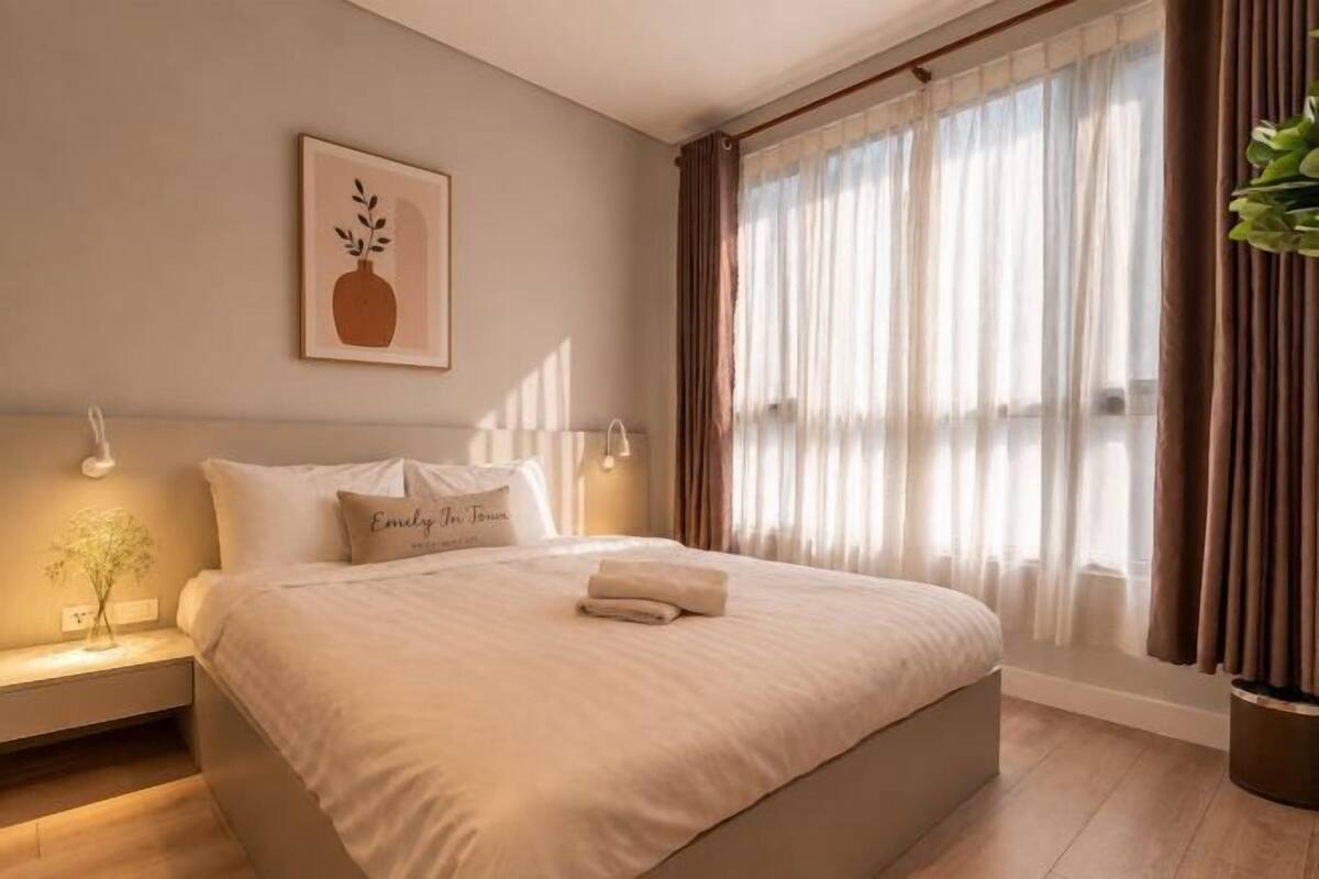 A neatly made bed with pillows, a bedside table with a lamp, and a window with curtains.