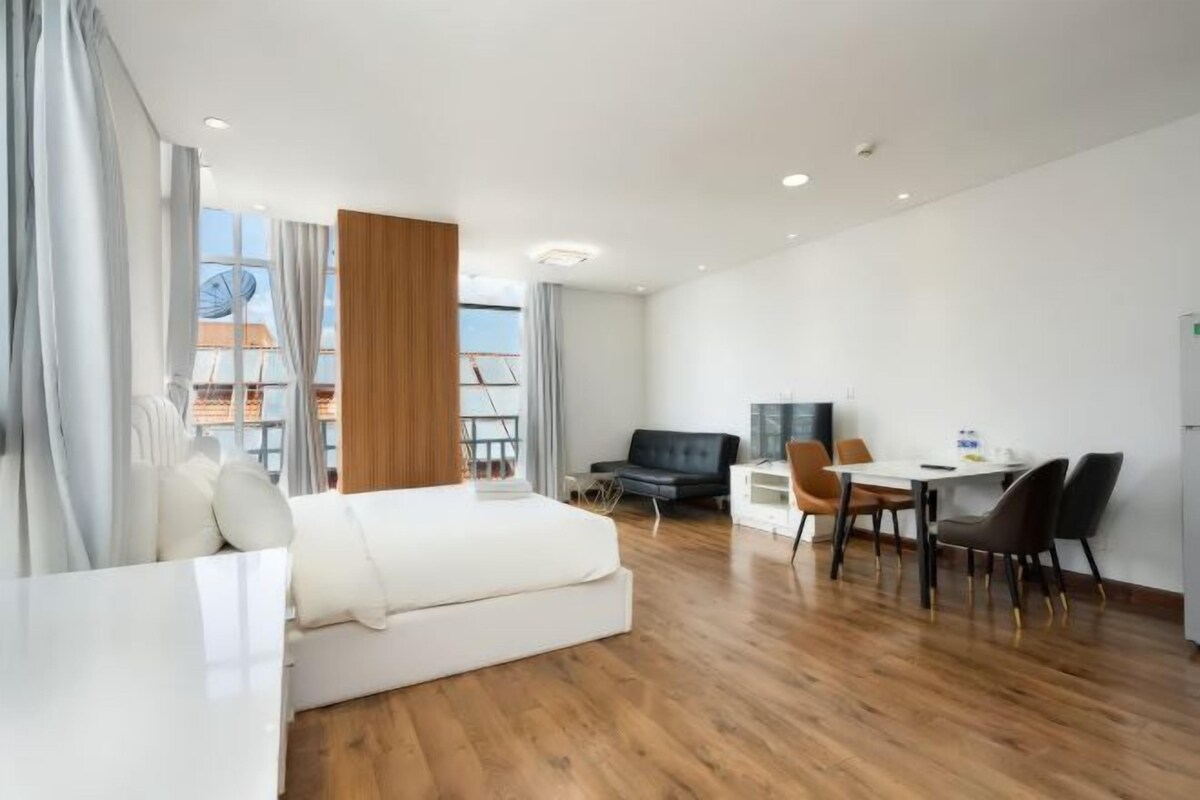 Habitación de hotel moderna con cama, escritorio y silla, una mesa de comedor y vista a la ciudad.