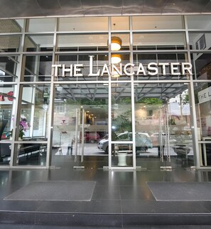 La façade de l’hôtel Lancaster, avec ses grandes fenêtres en verre et son panneau indicateur bien visible.