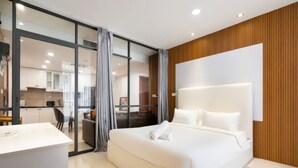 Habitación de hotel moderna con una cama grande, un escritorio y un ventanal corredero que da a una zona de cocina.