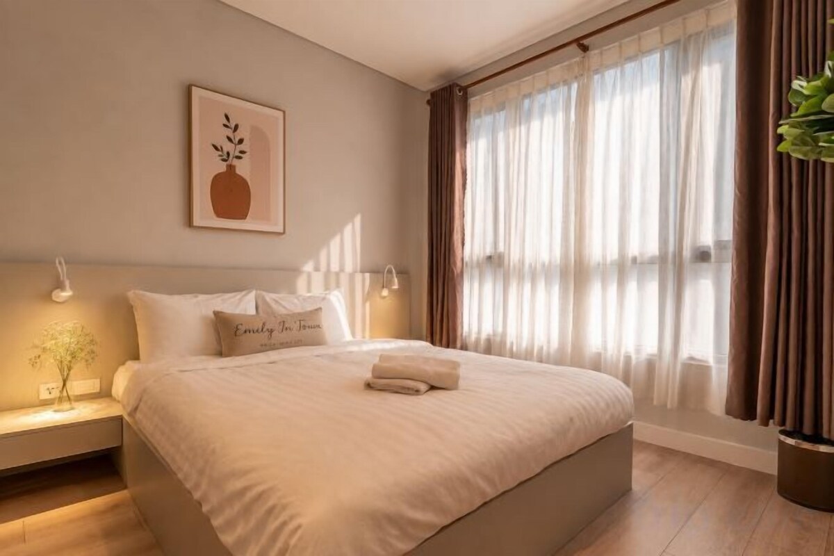 Un lit bien fait, avec des oreillers et une serviette pliée, une table de chevet avec une lampe et une fenêtre avec des rideaux.
