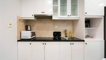 A modern kitchen with white cabinets, a black countertop, a microwave, a kettle, and a sink.