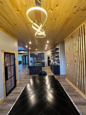 A modern interior with a wooden ceiling, a central black herringbone floor, and a kitchen area with blue cabinets and stainless steel appliances. - The Oslo + The Little Oslo Apt - 6 Kings + View + Hot Tub - Sleeps 27 (Jasper)