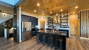 Une cuisine moderne avec des meubles de couleur sombre, des appareils en acier inoxydable et un îlot central doté de tabourets de bar.