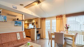 Ein gemütlicher Wohnbereich mit einer Couch, einem Esstisch mit Stühlen, einer Küchenzeile und einem Fenster mit Vorhängen.
