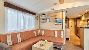 Ein kompakter Wohnbereich mit einer Couch, einem kleinen Tisch, einer Küchenzeile und einer Wand mit Fotos und einer Uhr.