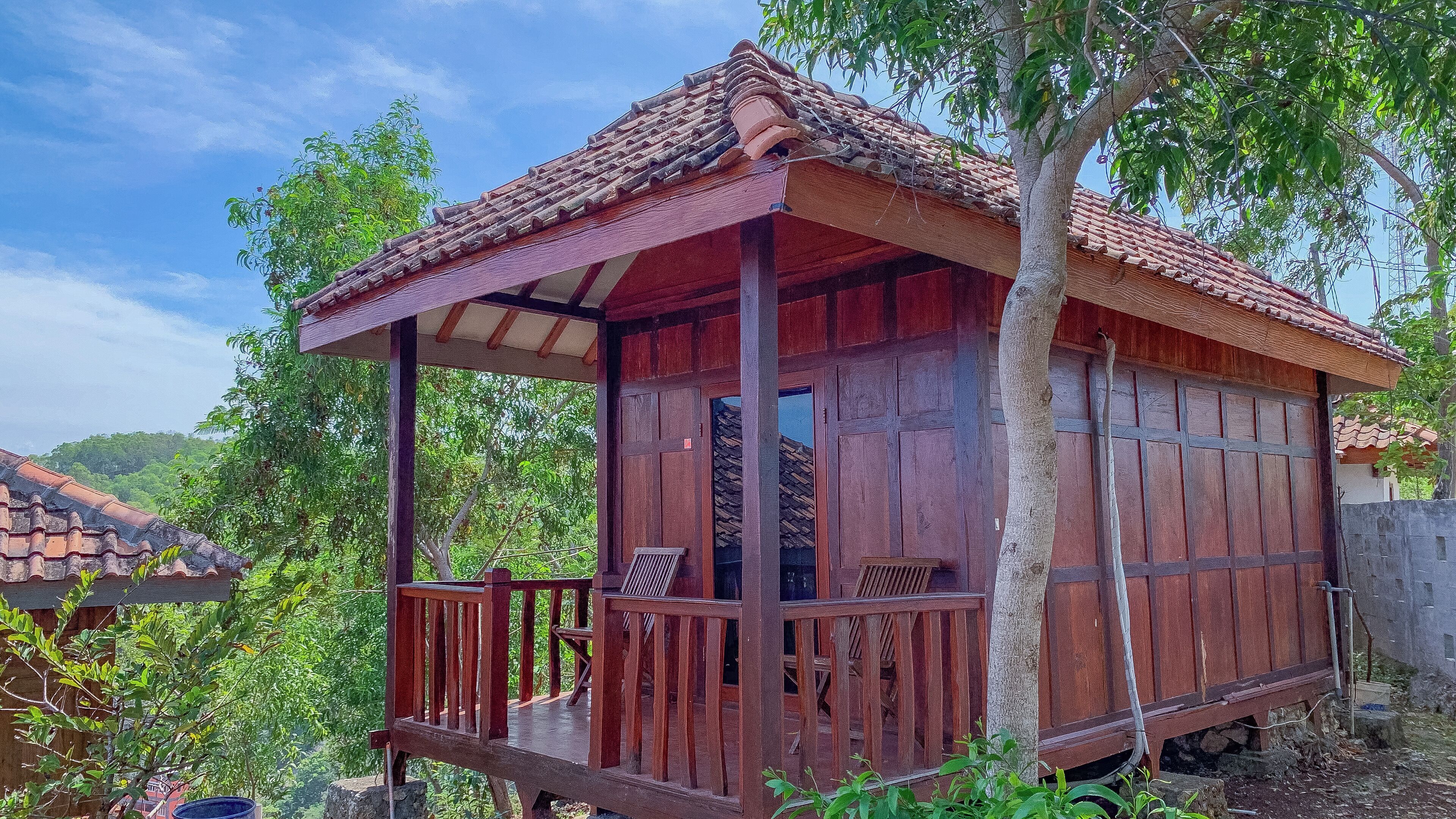 Una cabaña de madera con techo de tejas, un porche con barandilla y una puerta.