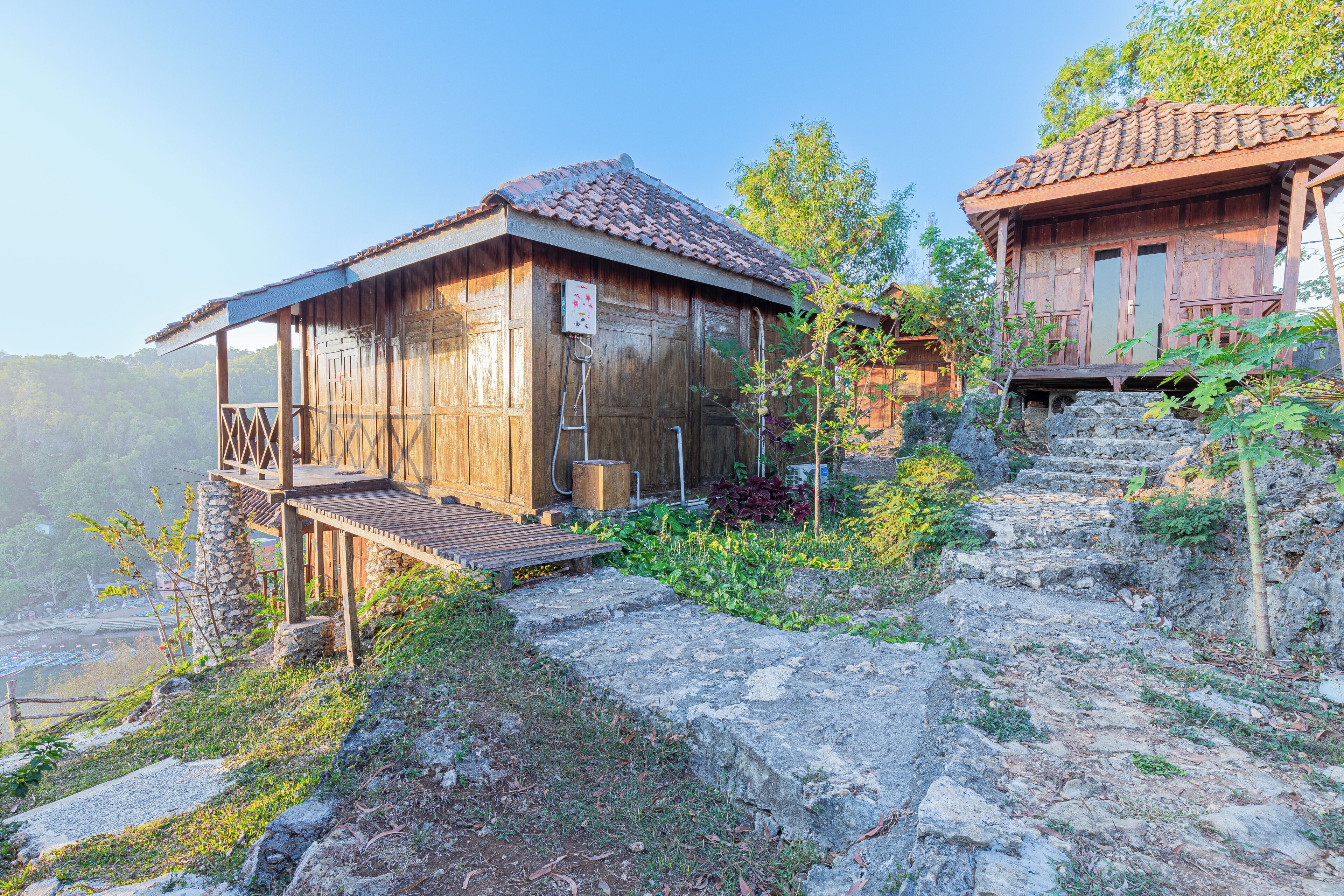 A rustic wooden cabin with a balcony, situated on a rocky hillside with a view of the valley below.