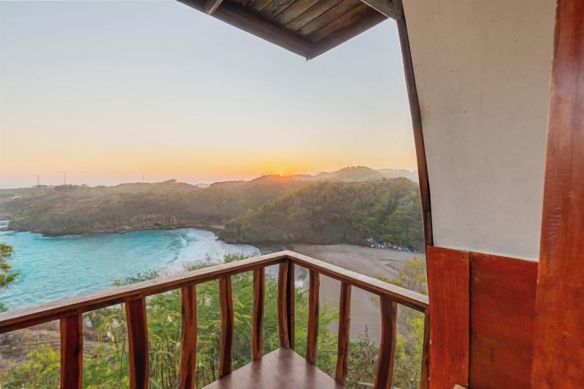A wooden balcony with a view of a coastal landscape during sunset.