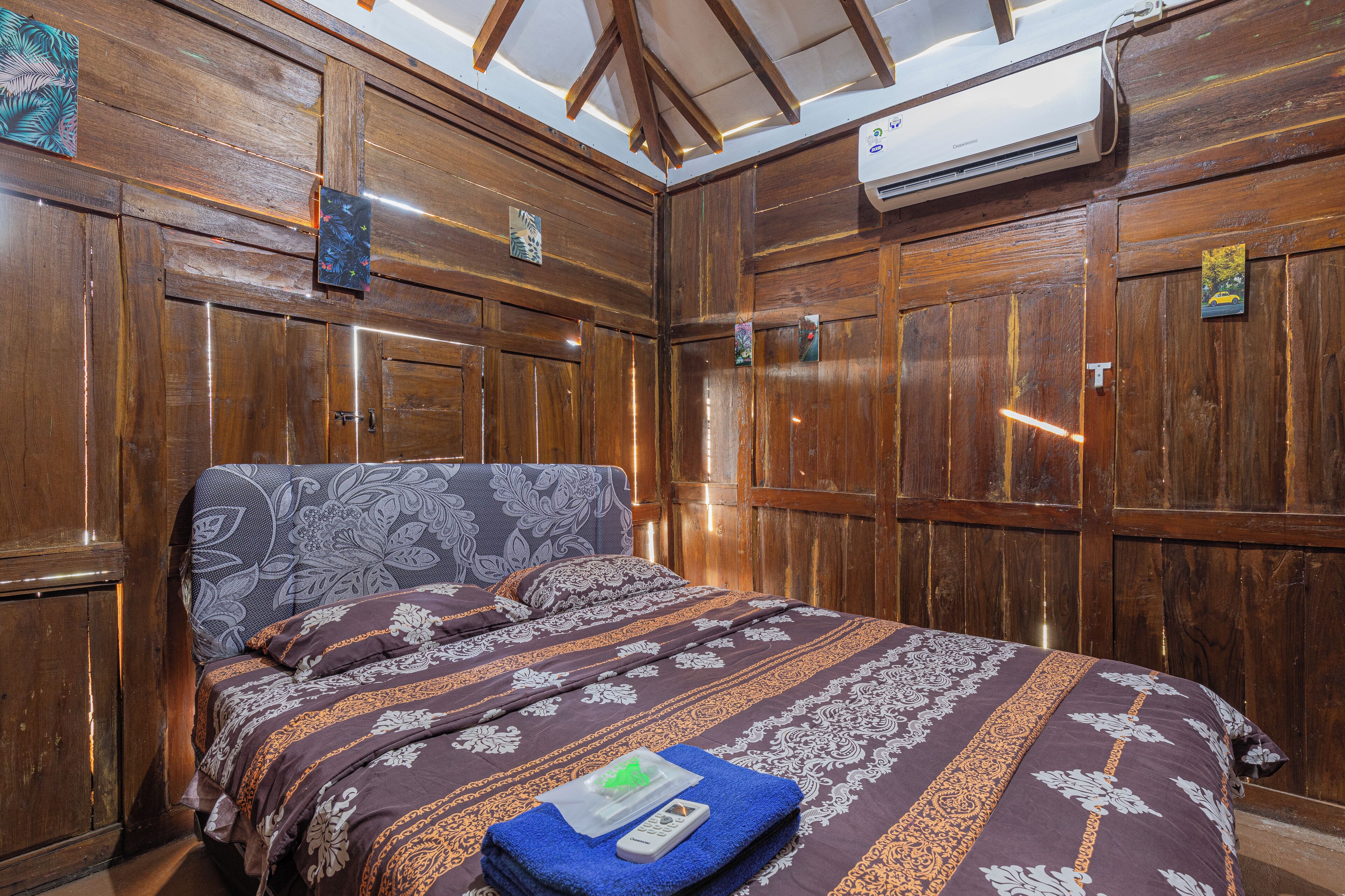 Habitación con paneles de madera, una cama, aire acondicionado y un pequeño cuadro en la pared.