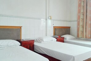 Una habitación de hotel con dos camas individuales, una mesita de noche roja, un cabecero de madera y una ventana con cortinas.