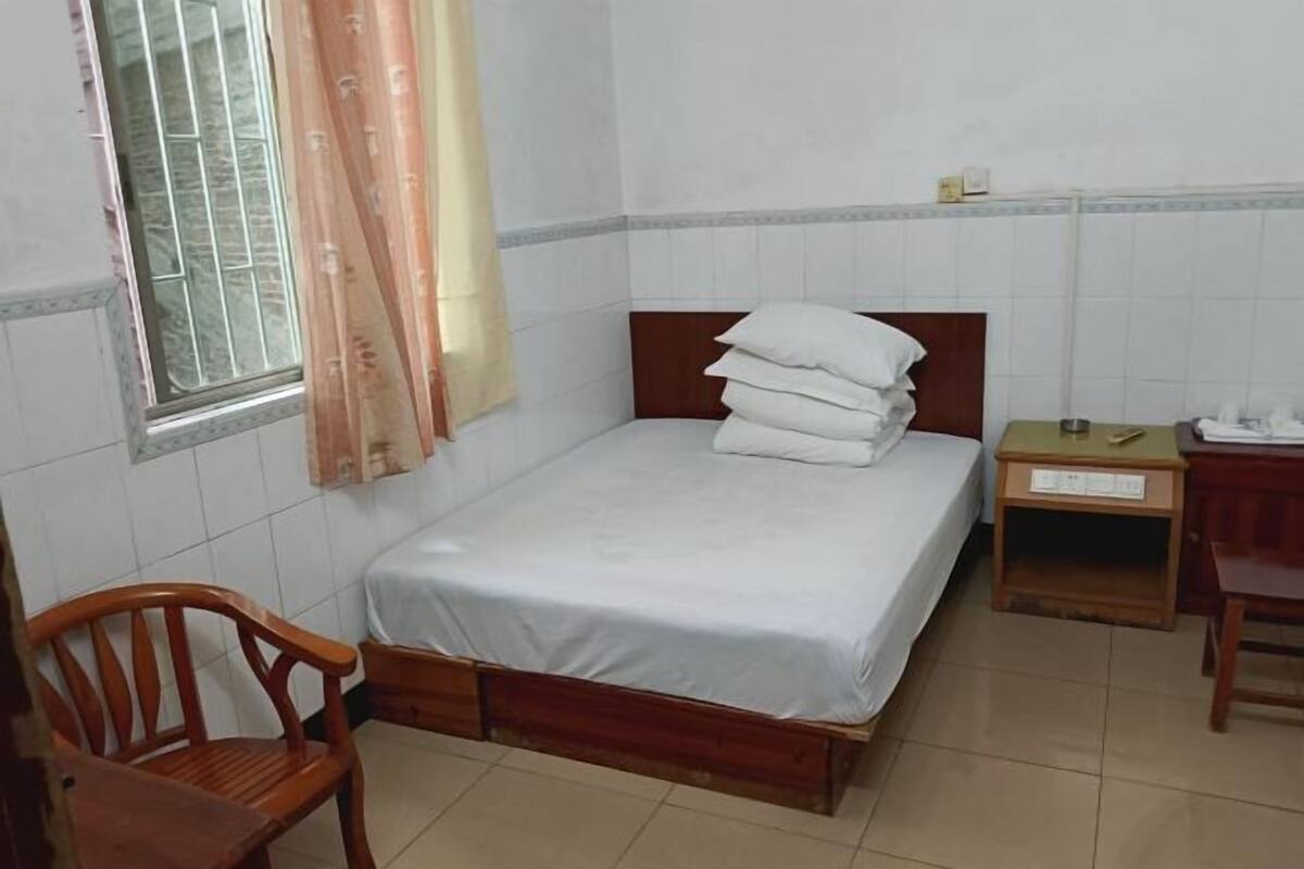 A single bed with a wooden headboard, a wooden chair, a small bedside table, and a window with a curtain.