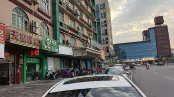 A street view with multiple commercial buildings, some with signage, and parked vehicles.