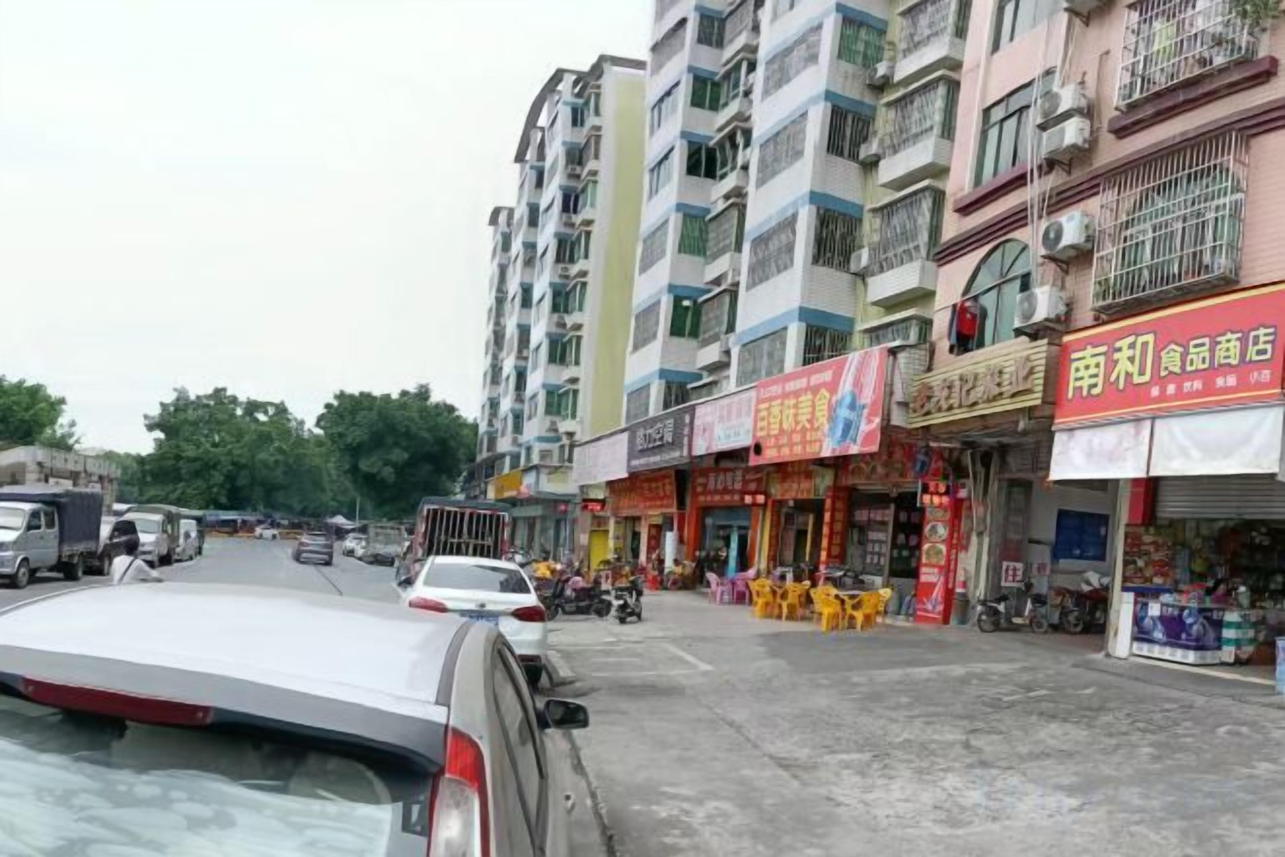 A street with multi-story buildings, shops, and parked vehicles.