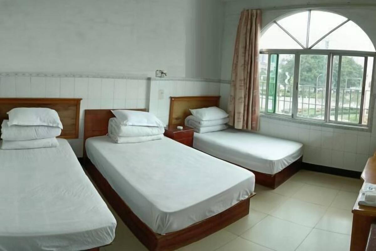 A room with three single beds, a large window with curtains, and a tiled floor.