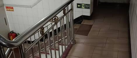 A corridor with a metal railing, tiled walls, and a fire extinguisher on the left.