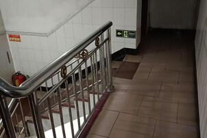 Un pasillo con barandilla de metal, paredes con azulejos y un extintor en la izquierda.