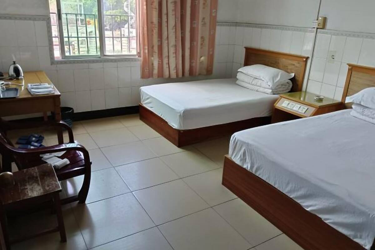 A hotel room with two beds, a desk, a chair, and a window with curtains.