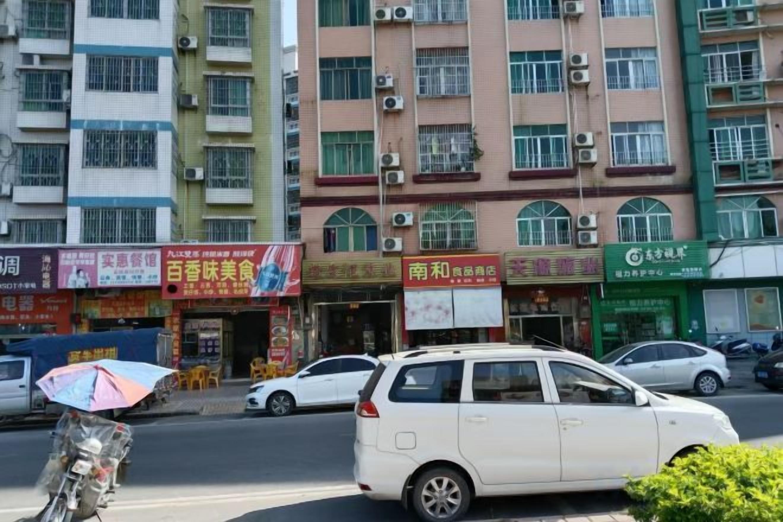 A street with buildings, a white car, and a person with an umbrella.