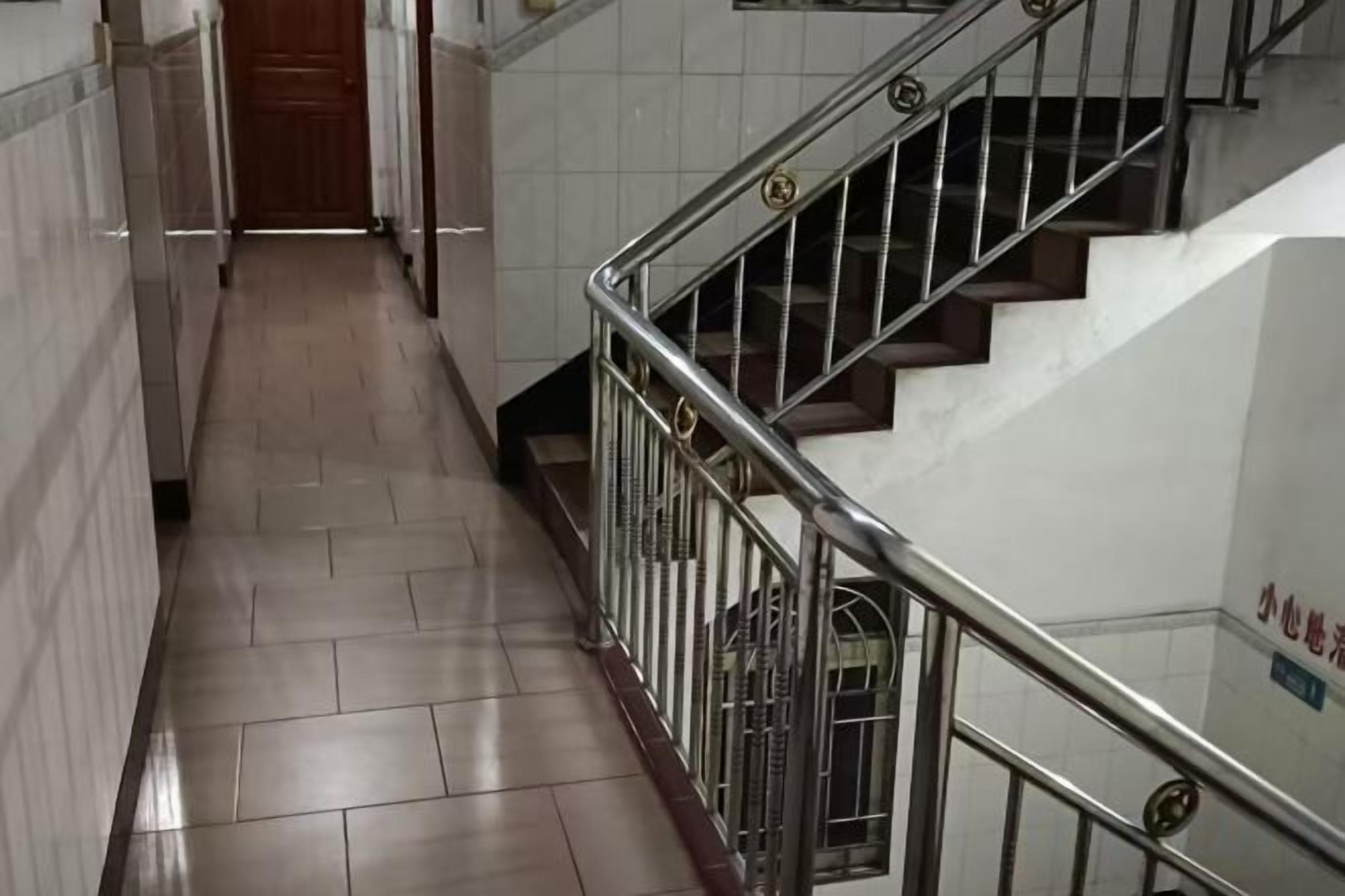 A corridor with a metal railing and a staircase with a wooden door at the end.