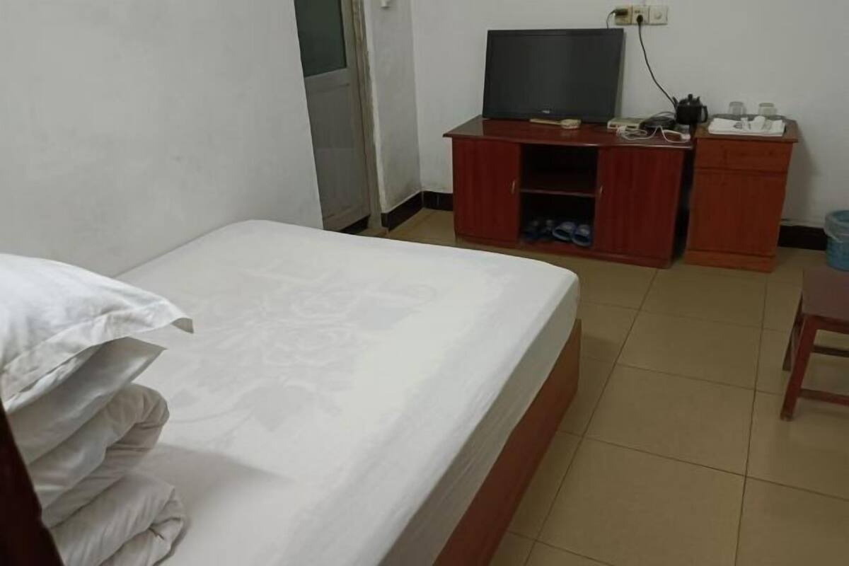 A hotel room with a bed, a TV on a wooden stand, and a small desk with a chair.