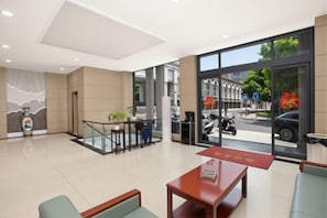 Un hall d’hôtel comprenant un comptoir d’accueil, un espace salon et de grandes fenêtres donnant sur la rue.