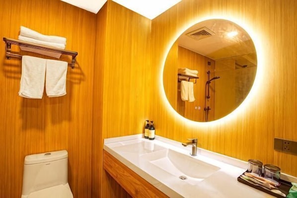 Un baño con pared de madera, un espejo redondo, un lavabo blanco y un inodoro.