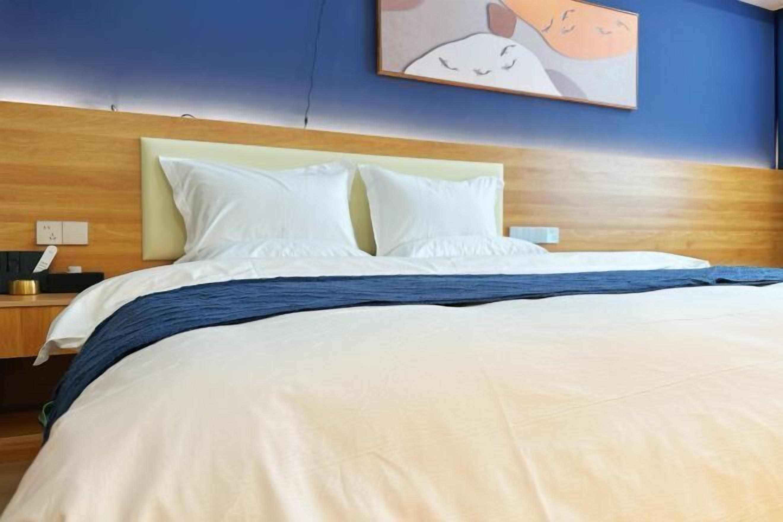 A neatly made bed with white and blue bedding, a wooden headboard, and a wall-mounted artwork.