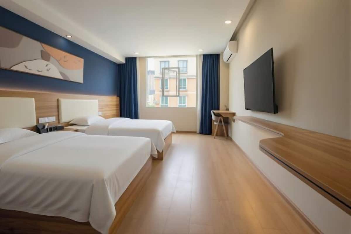 Ein Hotelzimmer mit zwei Betten, einem Schreibtisch, einem Flachbildfernseher und einem Fenster mit Vorhängen.