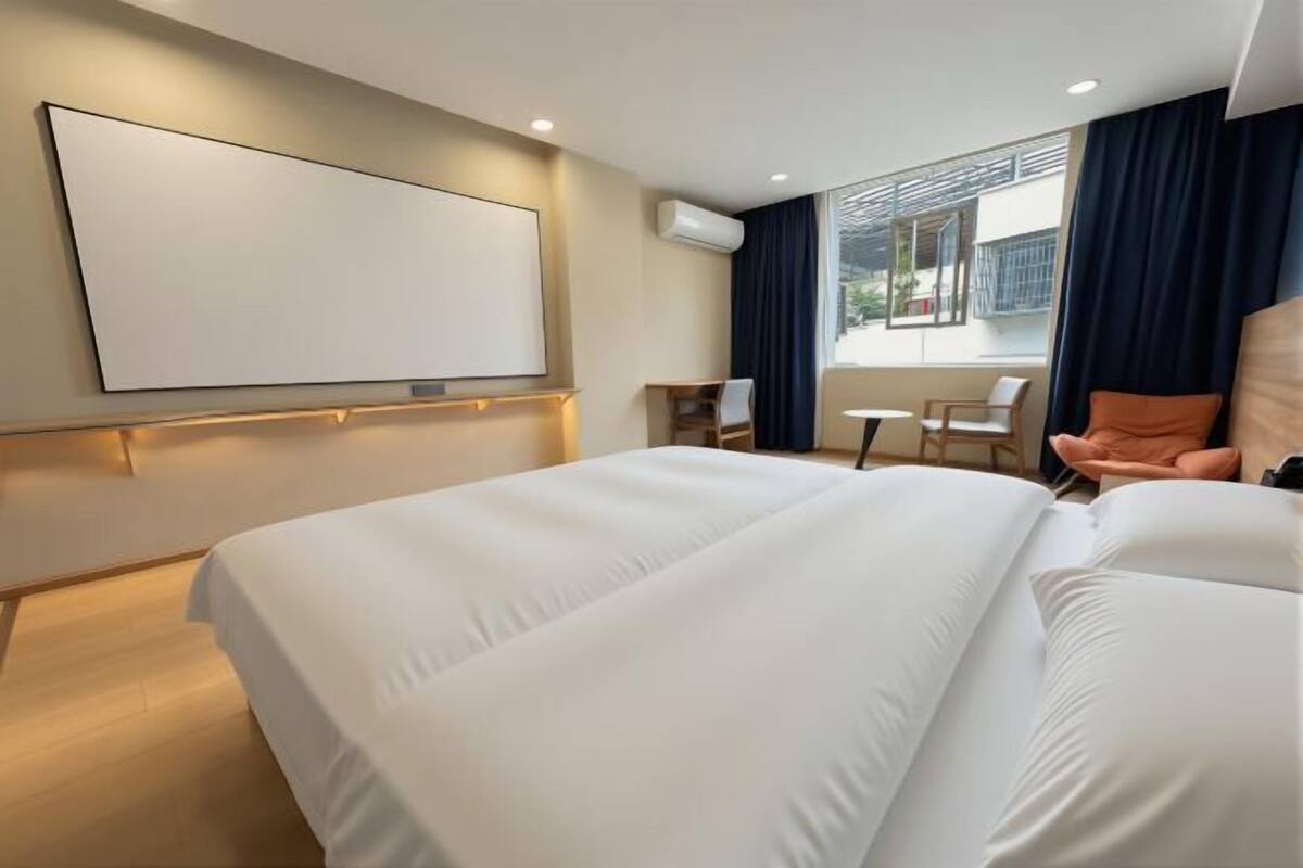 Ein Hotelzimmer mit einem großen Bett, einem Schreibtisch, einem Sessel, einem Fernseher und einem Fenster mit Vorhängen.